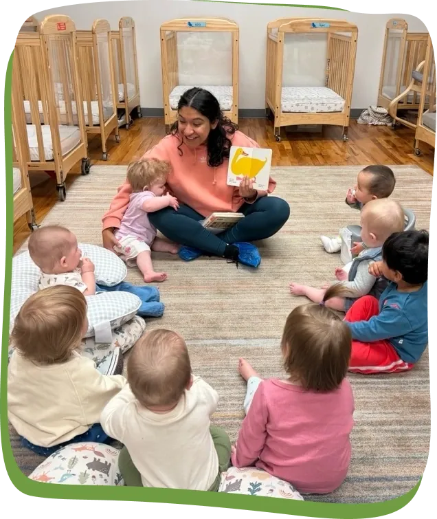 A Songbird Academy teacher reads a picture book to infants sitting on the rug beside the cribs