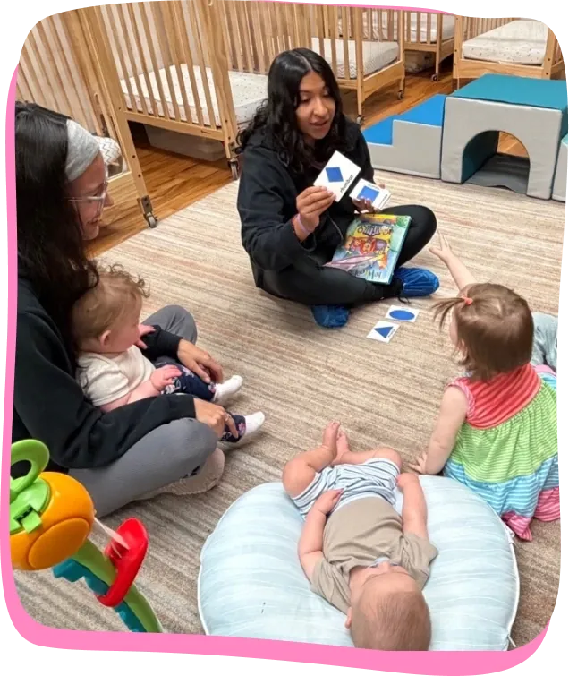 Two Songbird Academy teachers play with infants using shape cards in the infant room